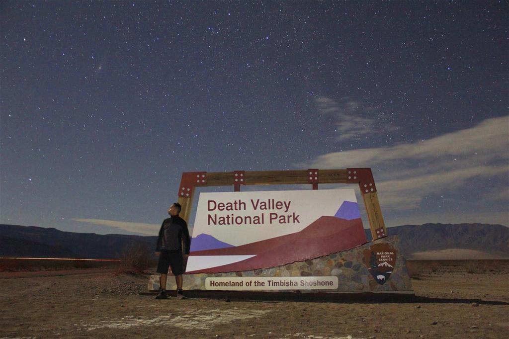 Standing next to the Death Valley sign on starry night with the Andromeda galaxy on left top of the picture. Winter 2013. California, USA.